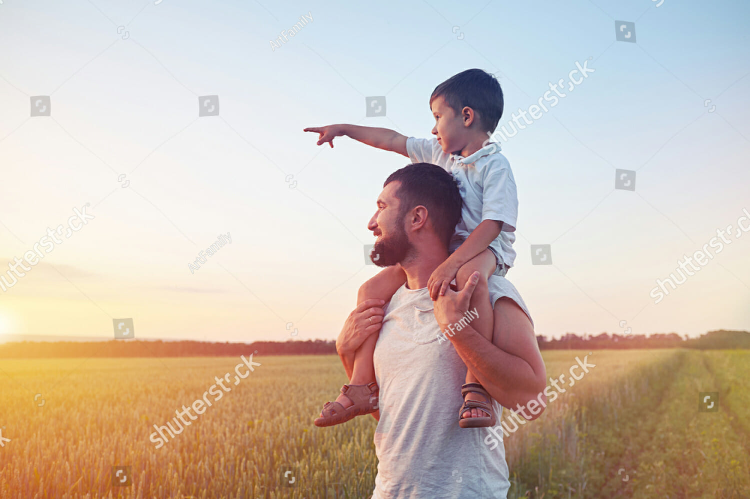stock-photo-small-boy-is-sitting-on-his-father-s-shoulders-and-pointing-at-the-sun-in-the-field-during-451022278