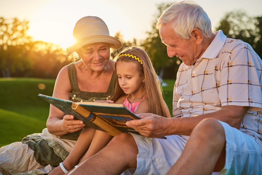 Retirement Planning - Grandparents Reading a Book with Granddaughter Outdoors, Enjoying Time Together at Sunset